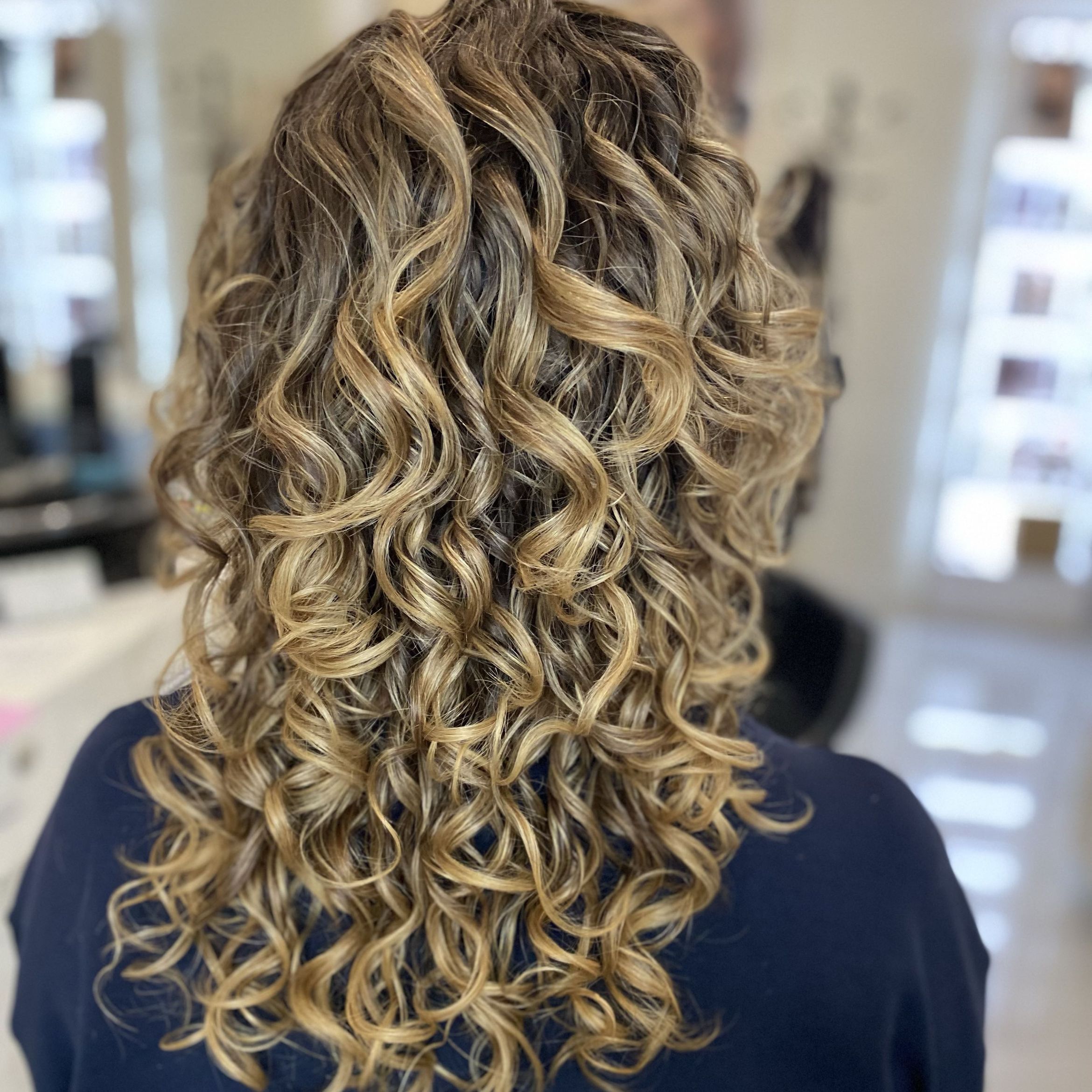 Blond loki z ciemniejszą nasadą, wyraźny skręt i objętość, ujęcie od tyłu.